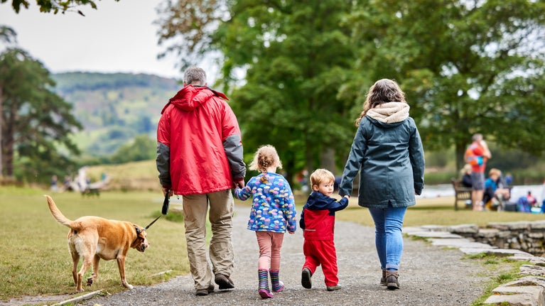 A family walking their dog along the lake front at Fell Foot Park